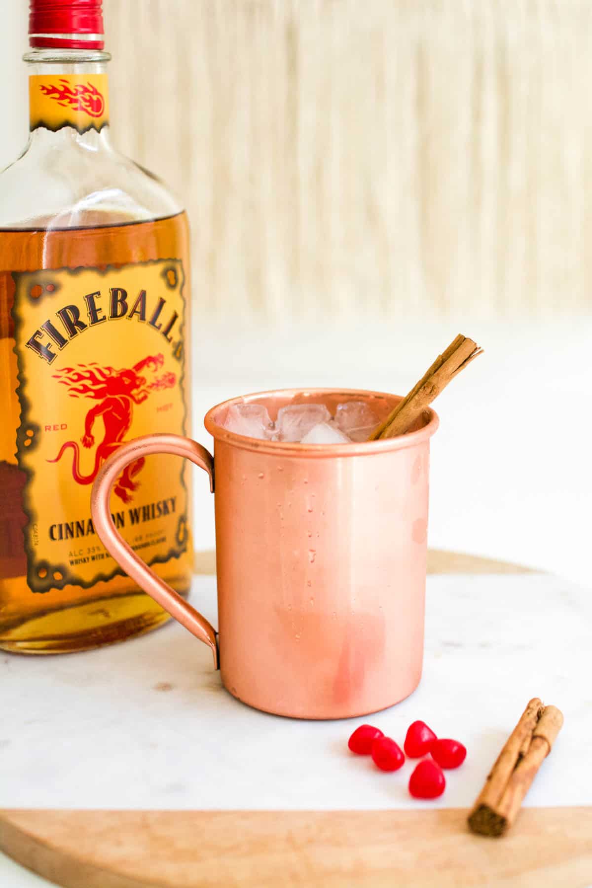 A bottle of Fireball with a copper cup holding a cocktail sitting on a table in front of it.