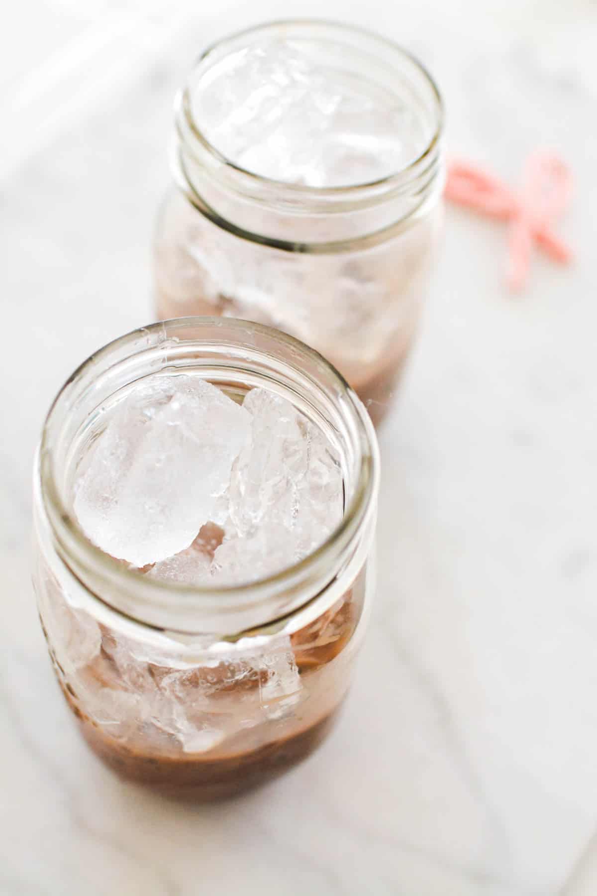 Overhead view of jars with chocolate syrup and ice on a counter.