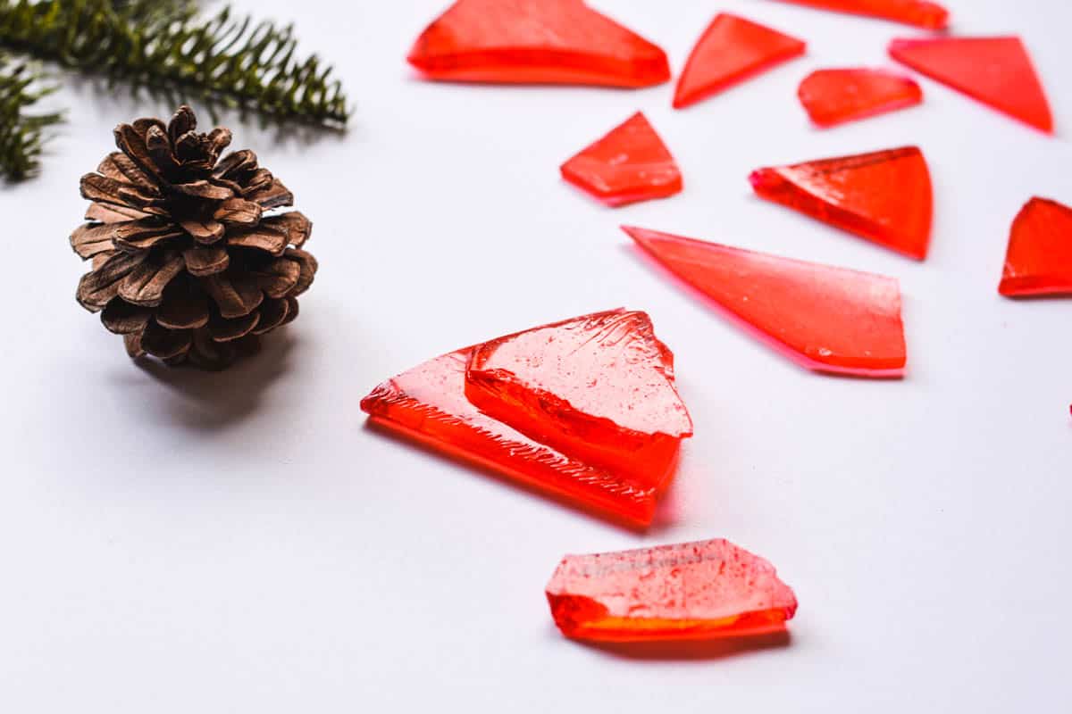 Pieces of red cinnamon hard candy on a table next to a pinecone.