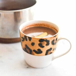 Leopard print mug filled with hot chocolate garnished with a piece of orange rind.