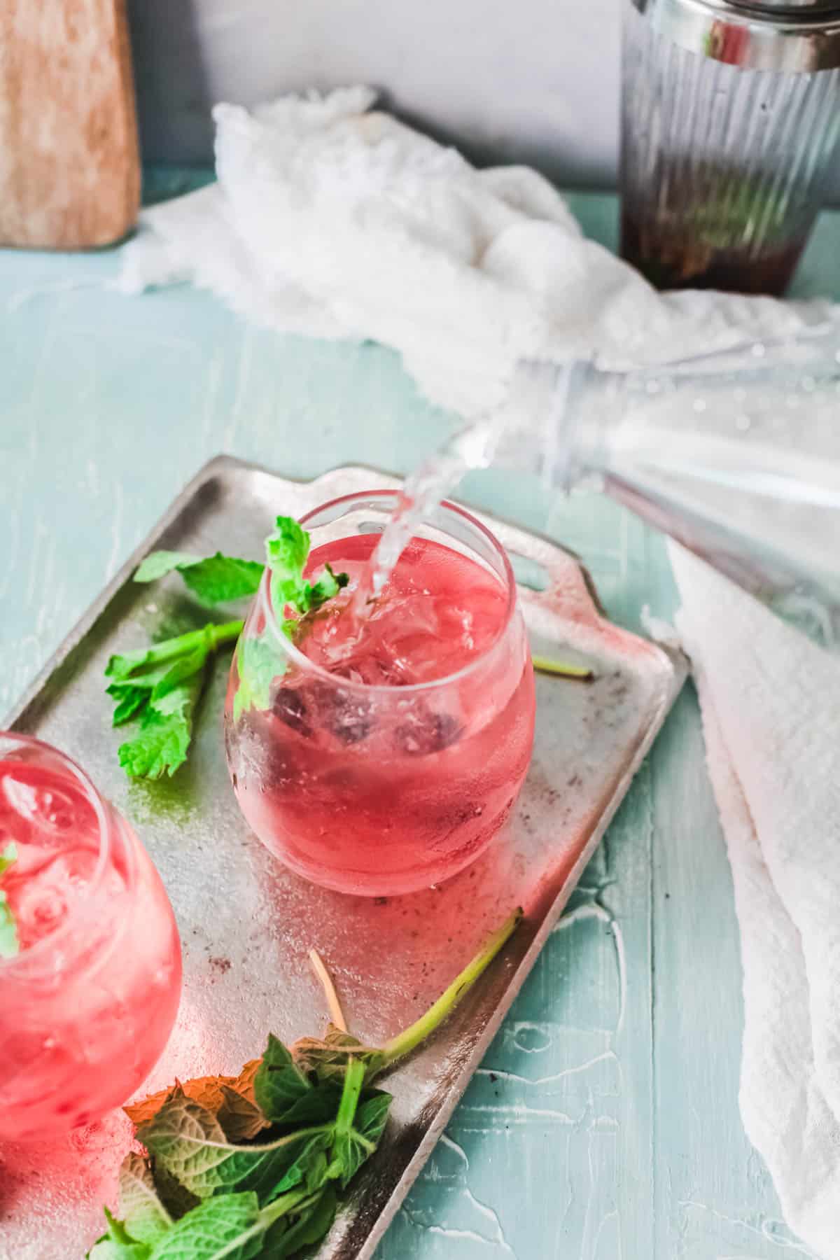 Club soda being poured into a cocktail in a stemless wine glass.