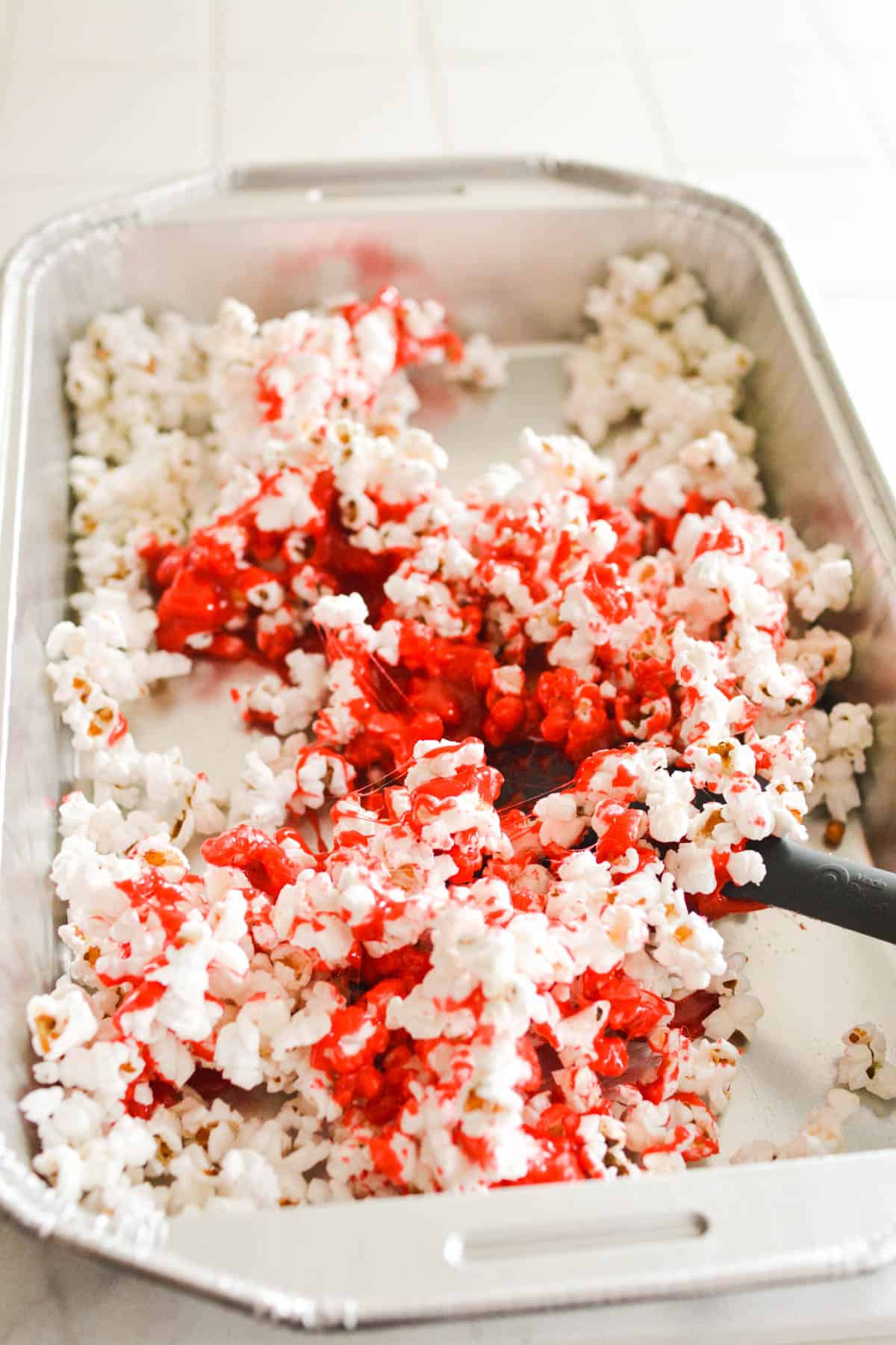 Popcorn in a baking pan starting to be coated in pink coating.