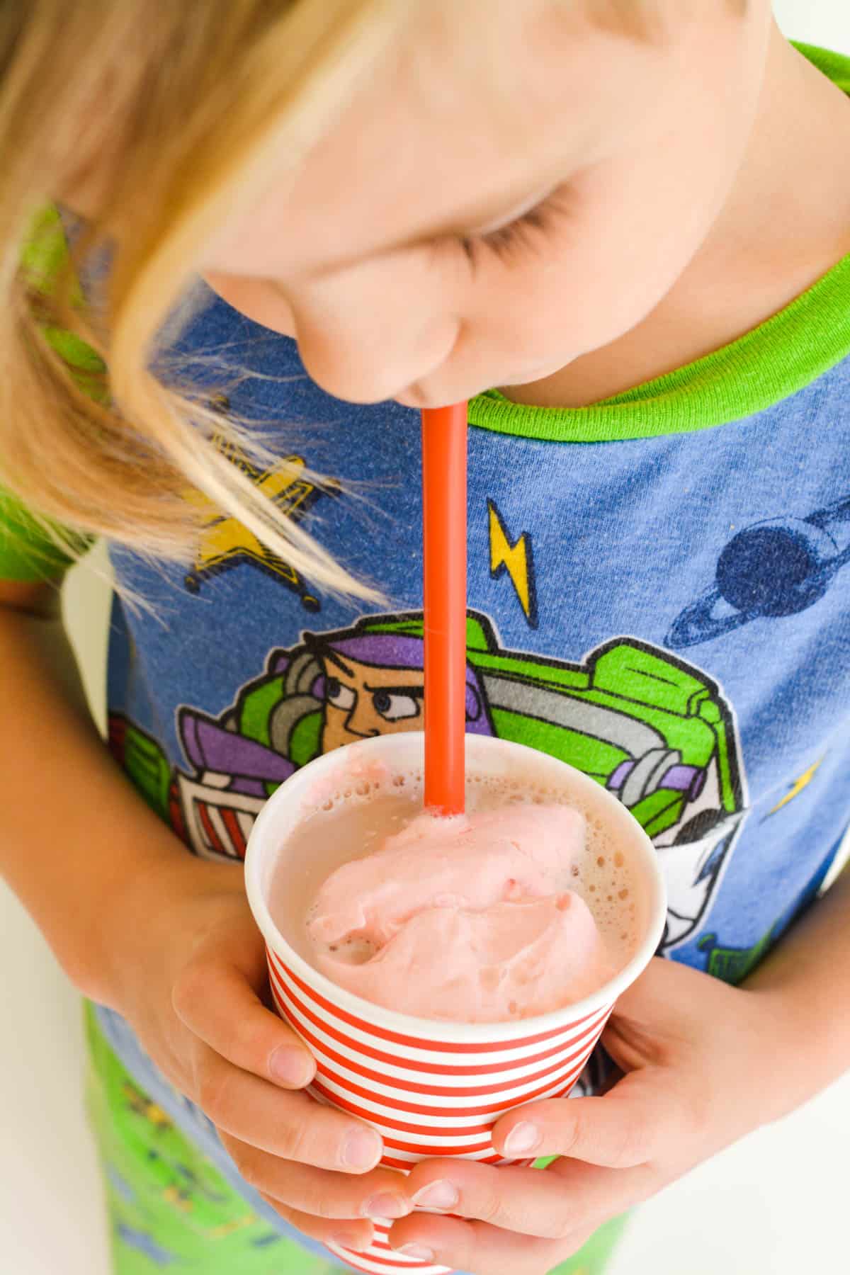 Kid drinking chocolate milk that is topped with cherry whipped cream.