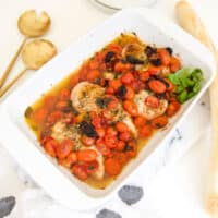 A baking dish with tomato topped chicken breasts on a table.