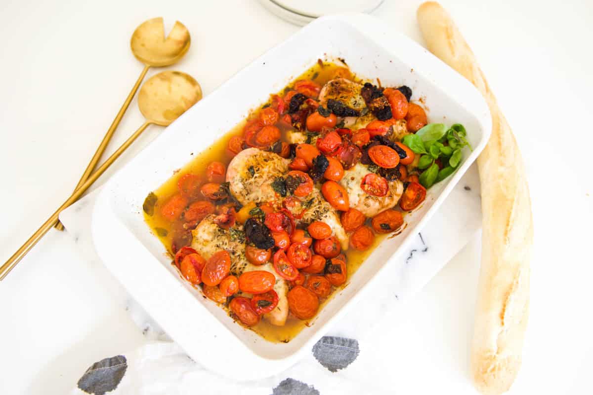 Close up of a baking dish holding baked chicken topped with a simple tomato bruschetta.