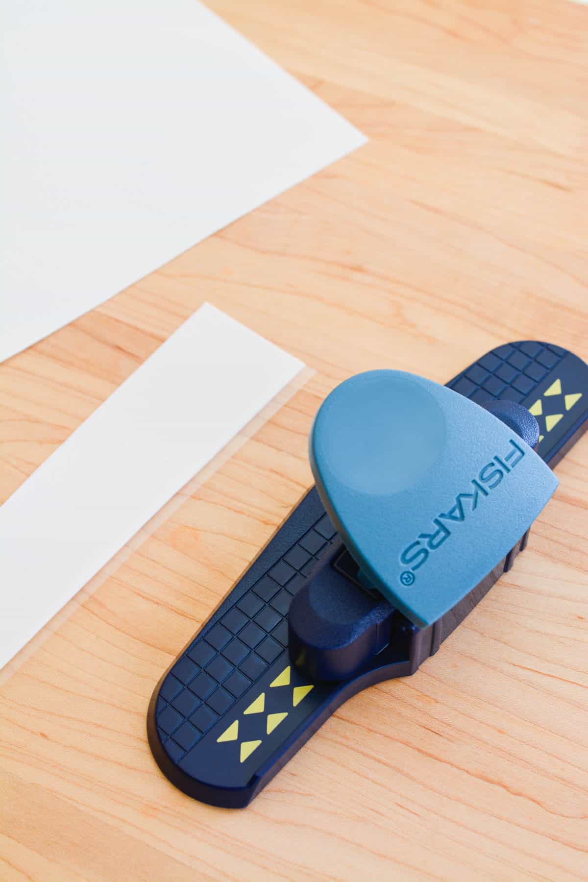 A decorative hole punch on a cutting board next to a sheet of edible decorative sheets.