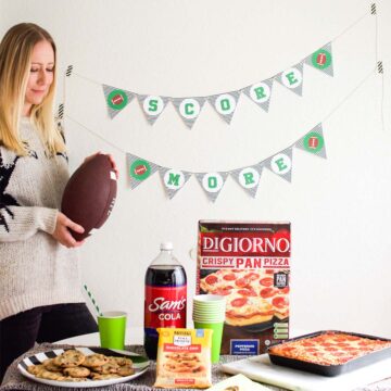 Woman standing next to a football banner and a table full of game day food.