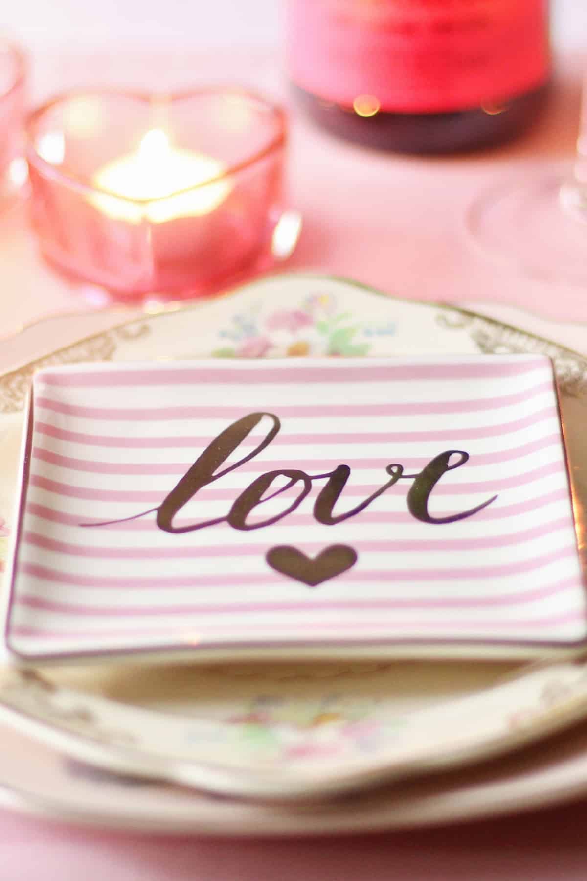 A small plate that says "love" on a table next to a candle.