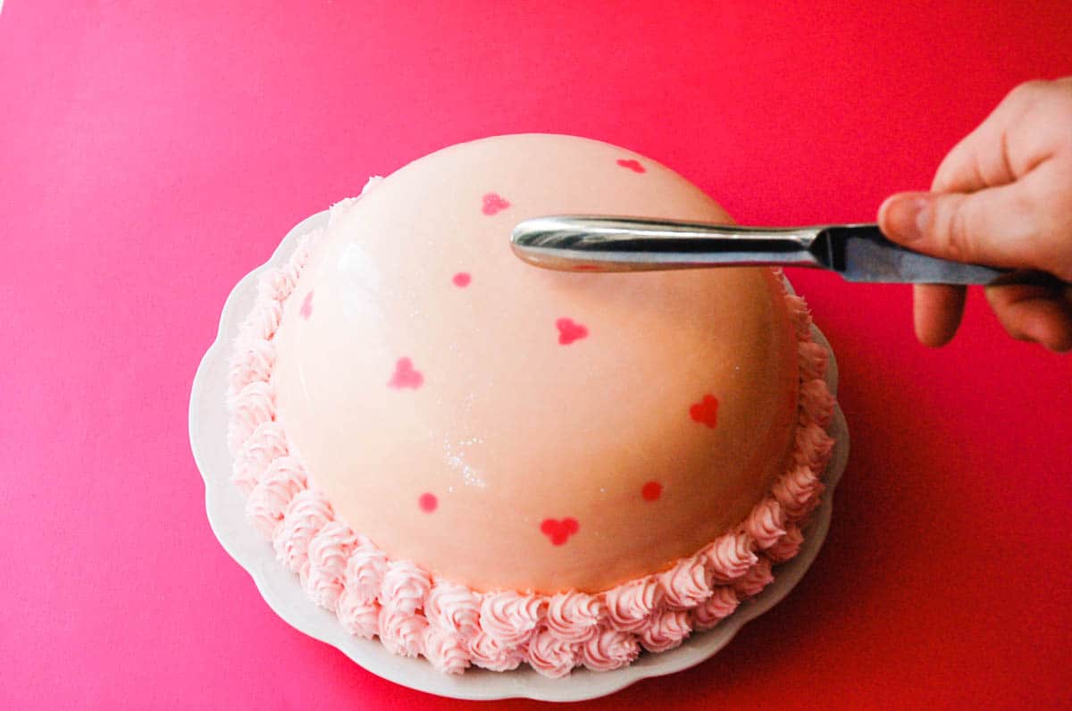 A girl using a knife to break a hard chocolate shell over a cake.