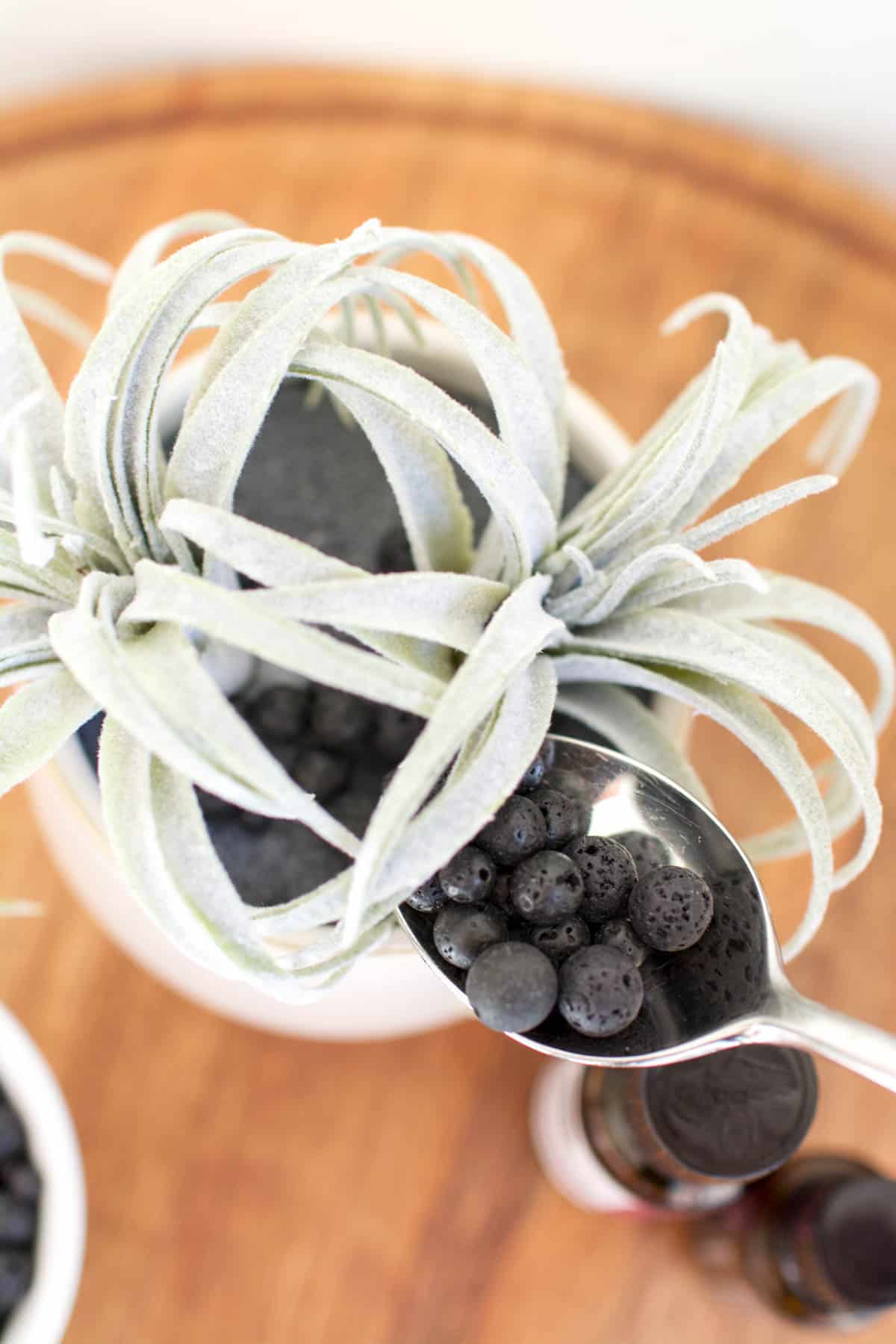 A spoon being used to add lava rocks to a faux succulent planter.