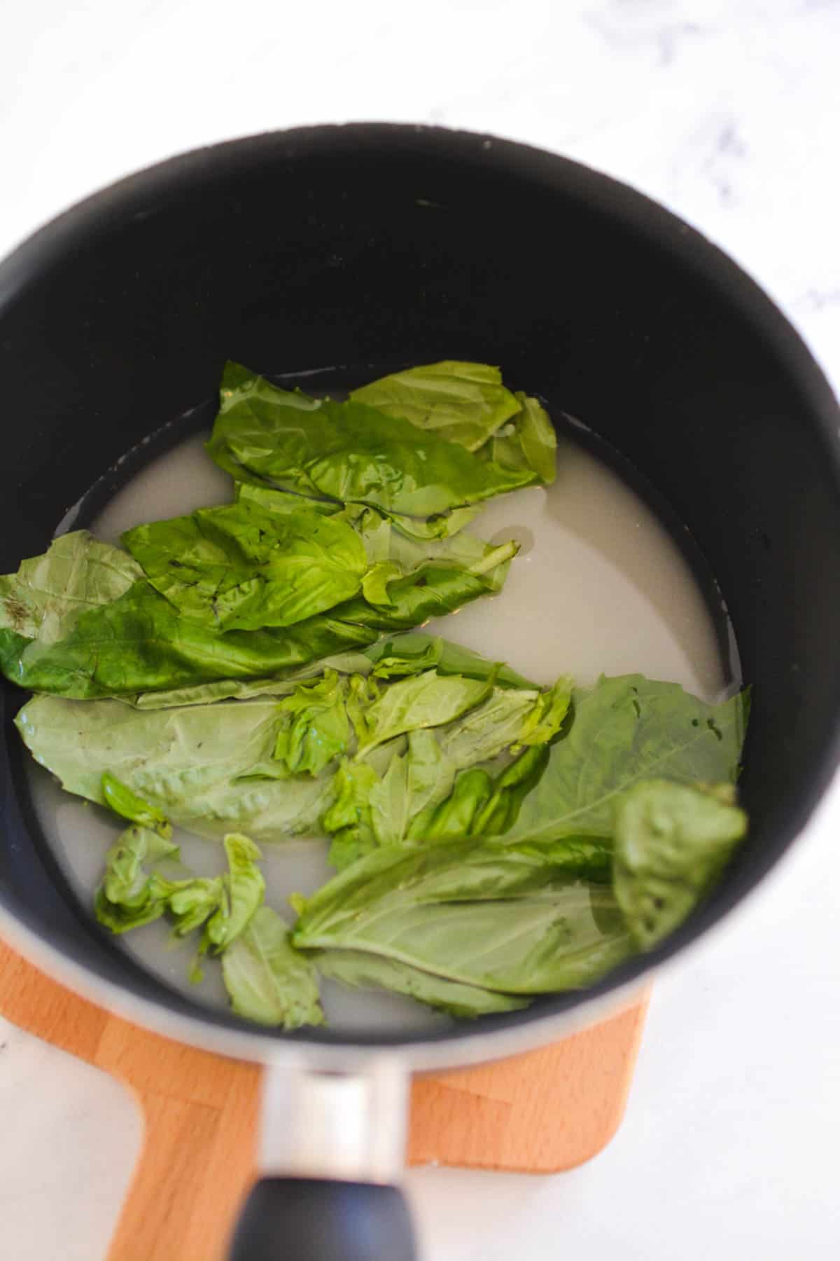 mixing in the sugar and water to the basil leaves on the stove 