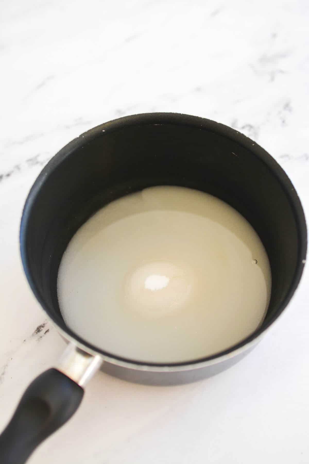 Saucepan with sugar and water on a counter.