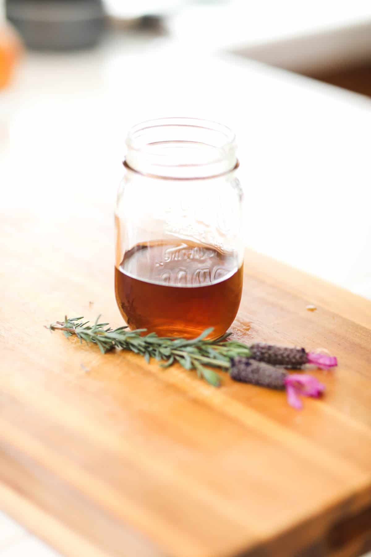 Lavender tea in glass jar on a counter with blooming lavender sprigs next to it.