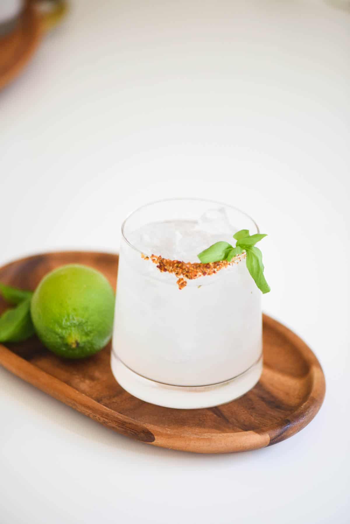 Margarita with basil and a smoky rim on a wooden tray next to a fresh lime. 