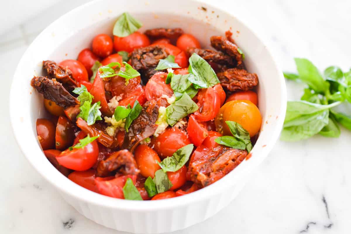 Close up of simple tomato bruschetta in a bowl next to some basil.