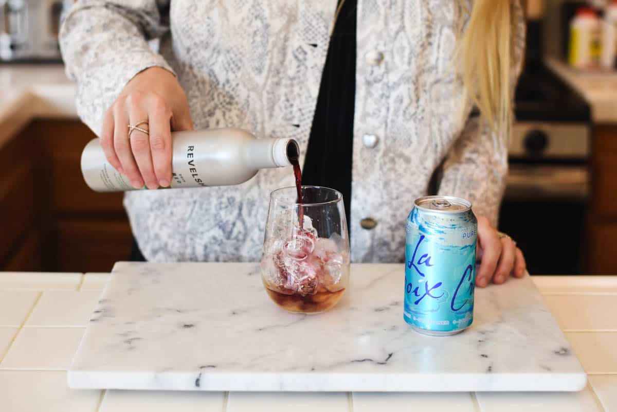 Woman pouring red wine into a stemless wine glass with ice in it.