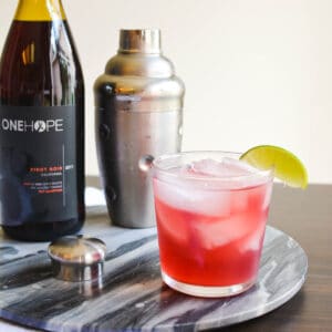 Close up of a tequila cocktail on a tray next to a cocktail shaker and wine bottle.