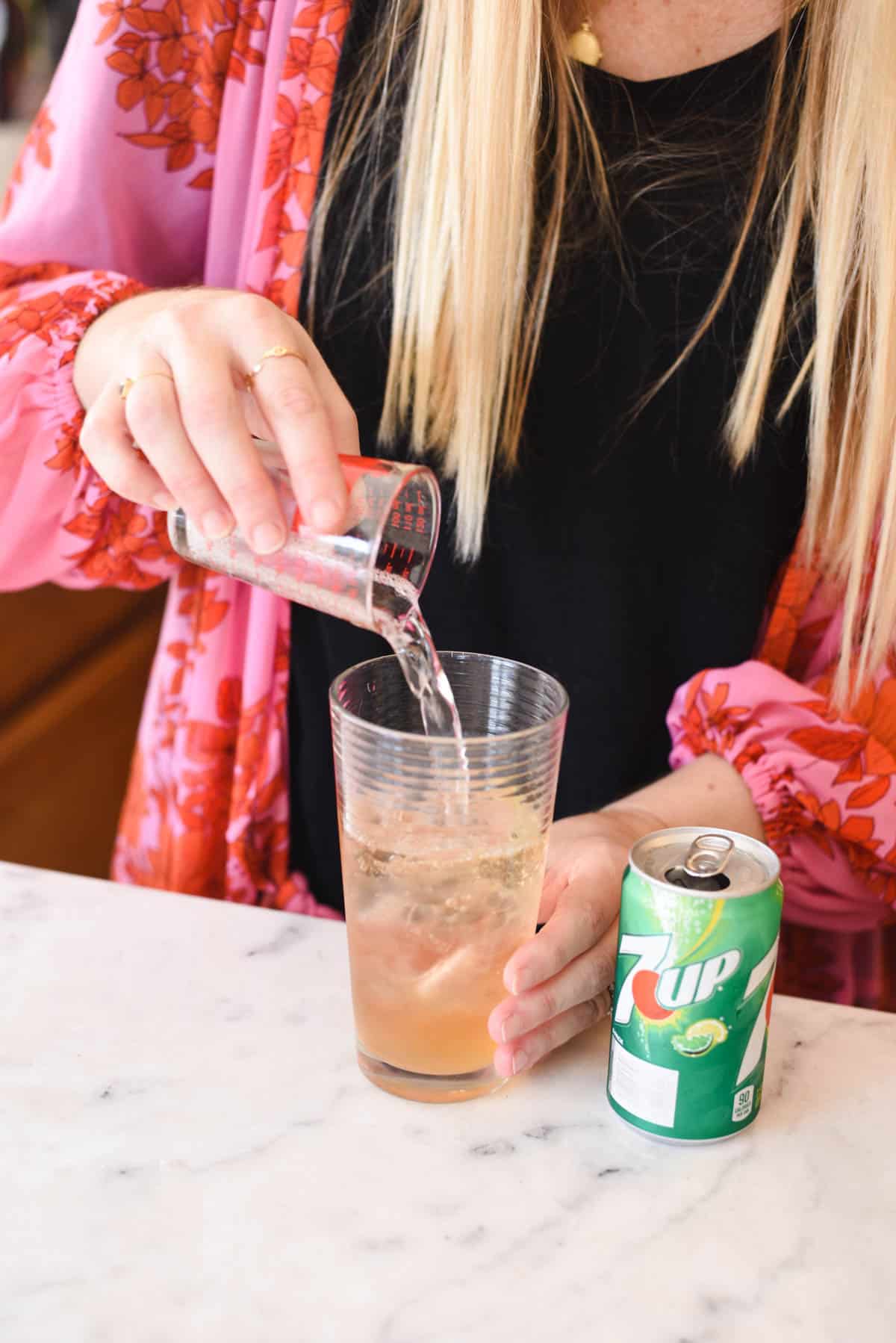 Woman using a glass measuring cup to add lemon lime soda to a cocktail glass.