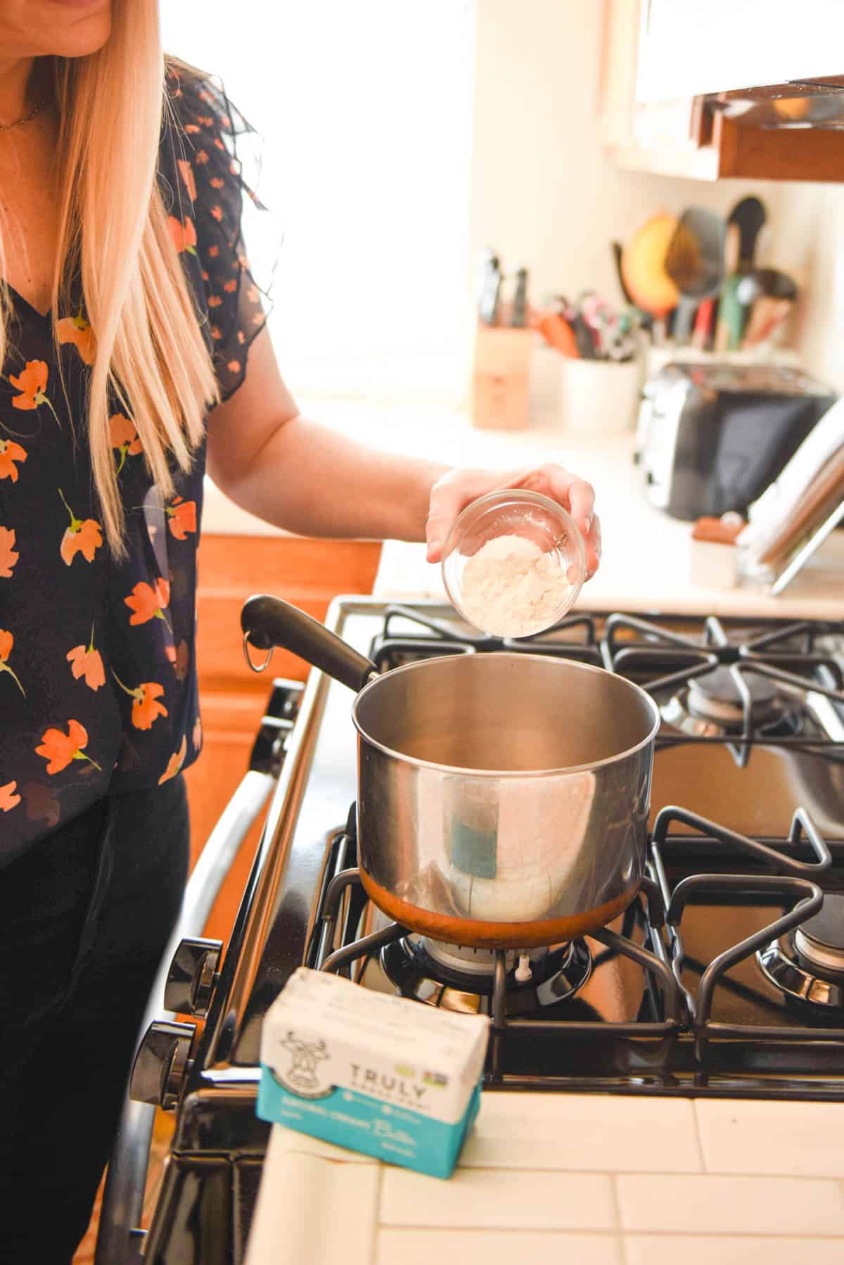 Woman adding flour to a saucepan.