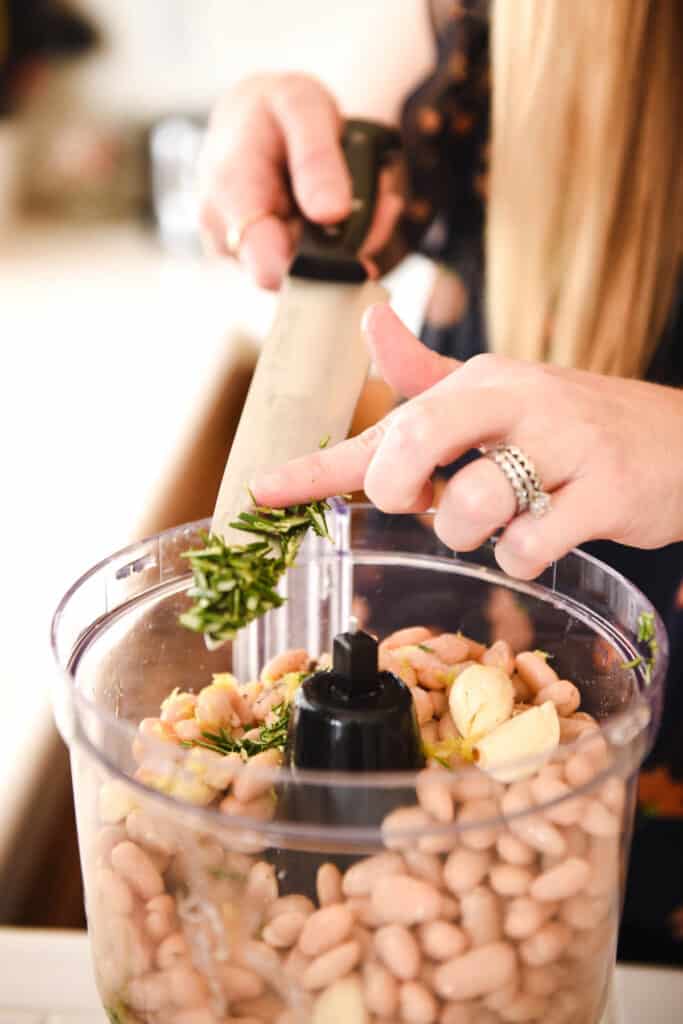 Woman adding chopped garlic to a food processor.