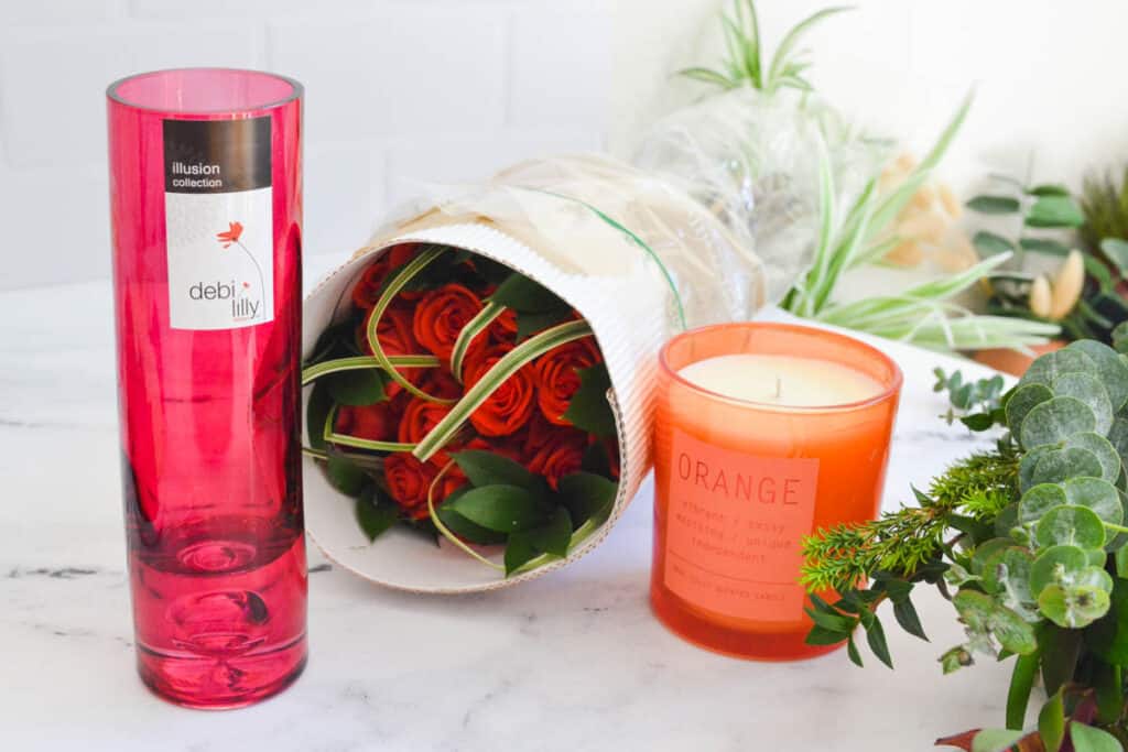 Close up of a pink vase, bouquet of roses and orange candle on a table.