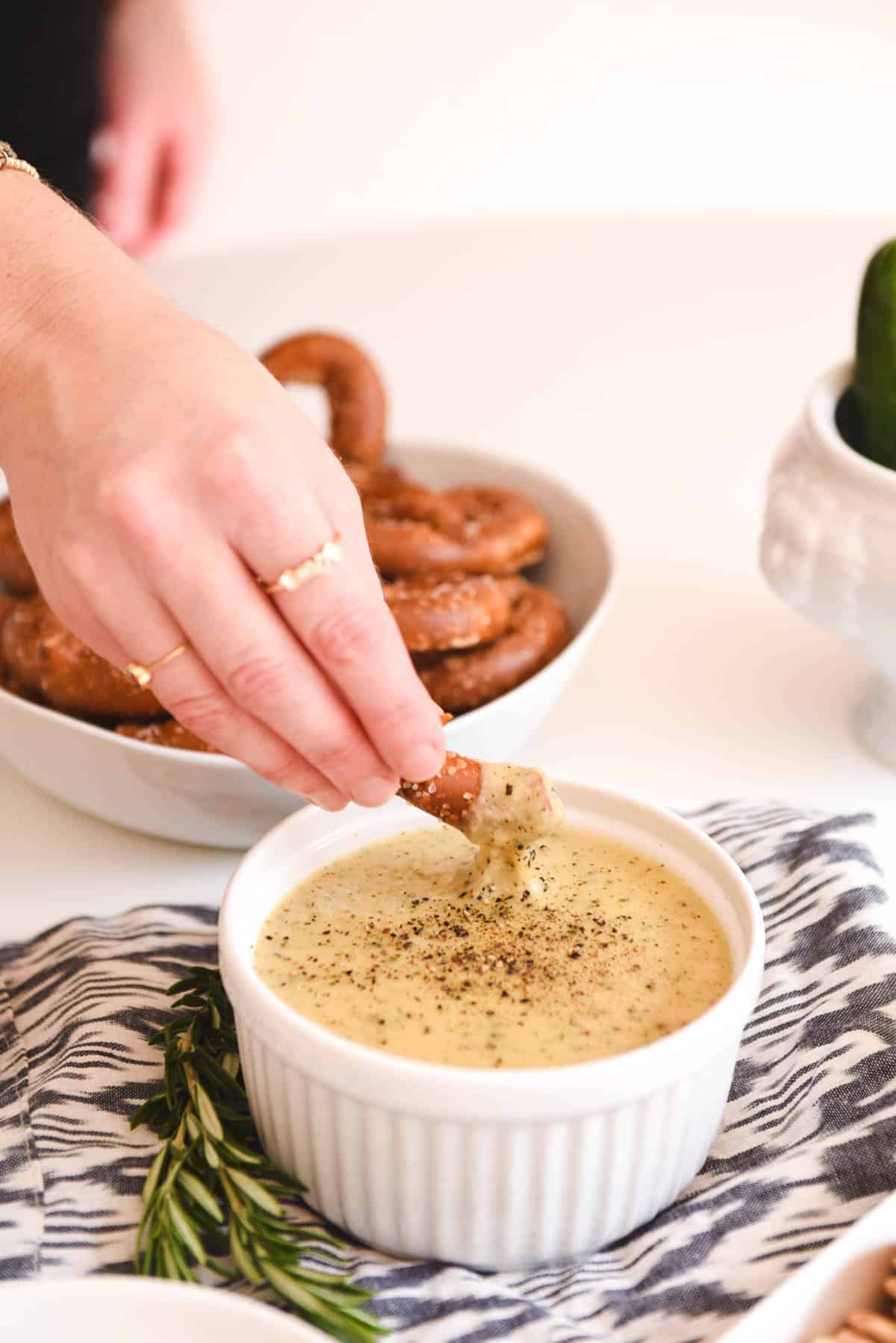 Close up of a woman scooping up beer cheese dip with a pretzel.