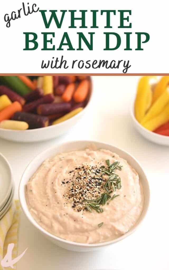 Close up of a white bowl holding a white bean dip topped with everything bagel seasoning and some rosemary.