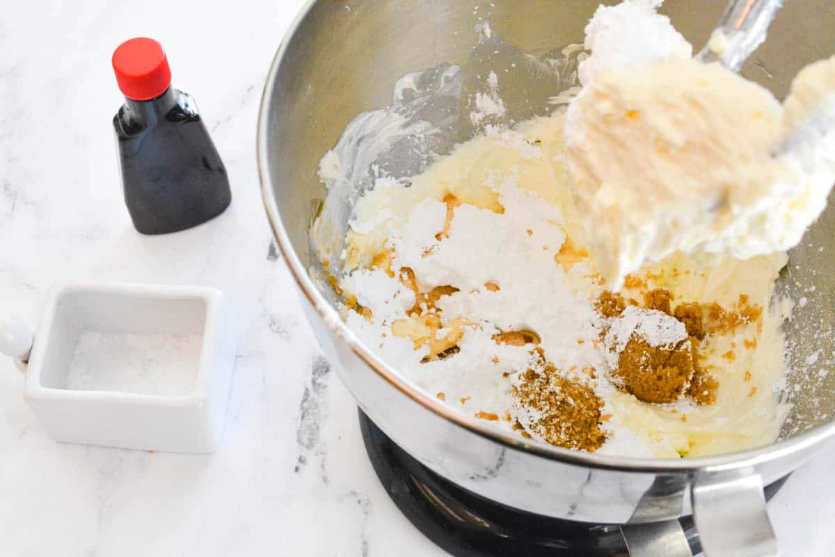 Ingredients in the bowl of a stand mixer with salt and vanilla on the counter next to it.