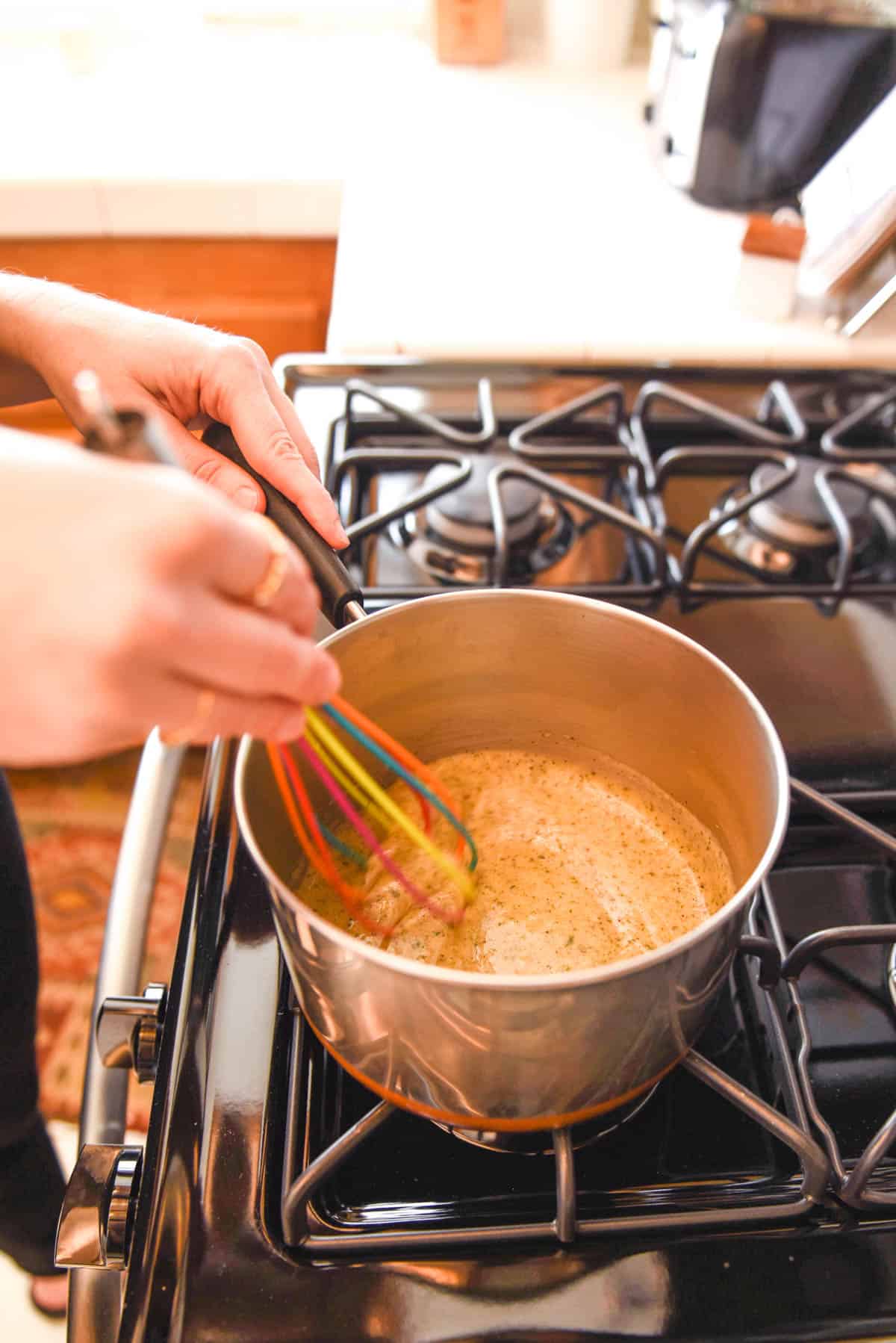 Woman stirring a dip with a whisk on the stove.