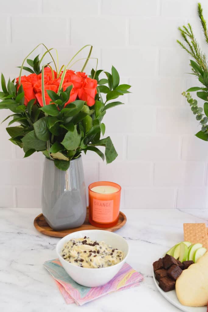 Valentine's Day table with fresh flowers in a vase next to a candle and a bowl of dessert dip.