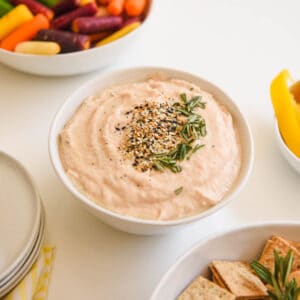 Close up of a bowl holding a dip topped with seasoning and rosemary.