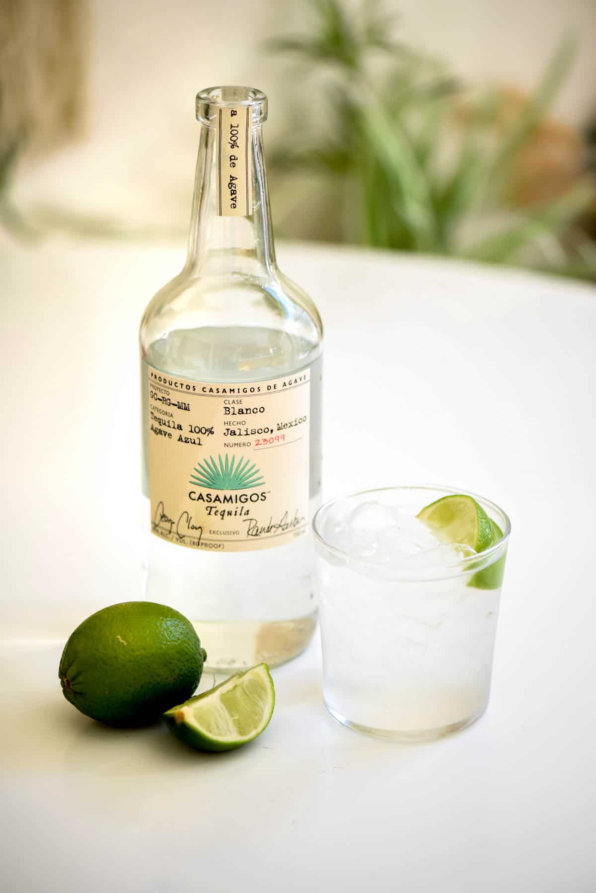 A short cocktail glass with Tequila Soda on a table next to a bottle of tequila and fresh lime.