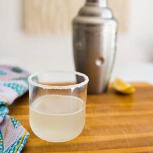 Lemon drop cocktail on wooden counter with cocktail shaker in the background.