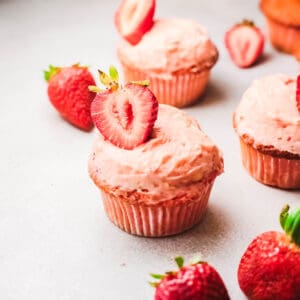 Close up of pink cupcakes with frosting and strawberry slices on top.