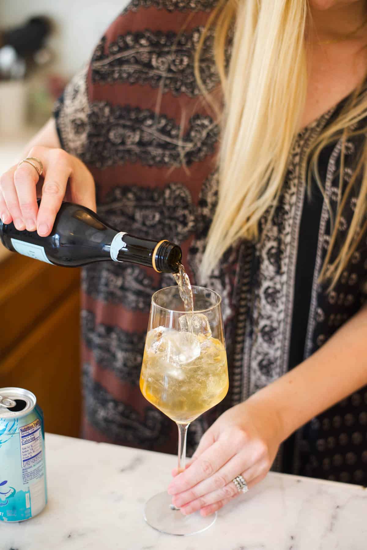 Woman adding champagne into a wine glass with other ingredients.