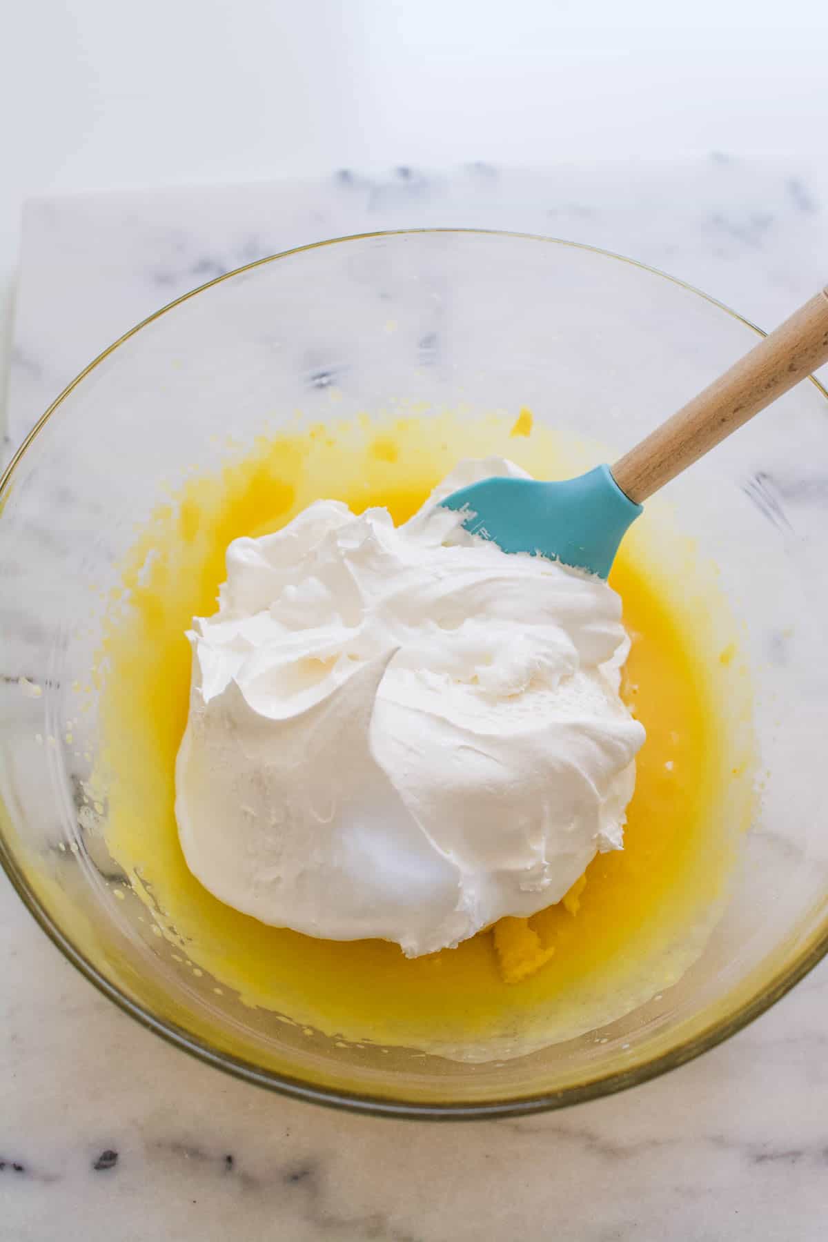 A bowl of vanilla pudding in a large glass bowl with Cool Whip on top and a spatula sticking out.