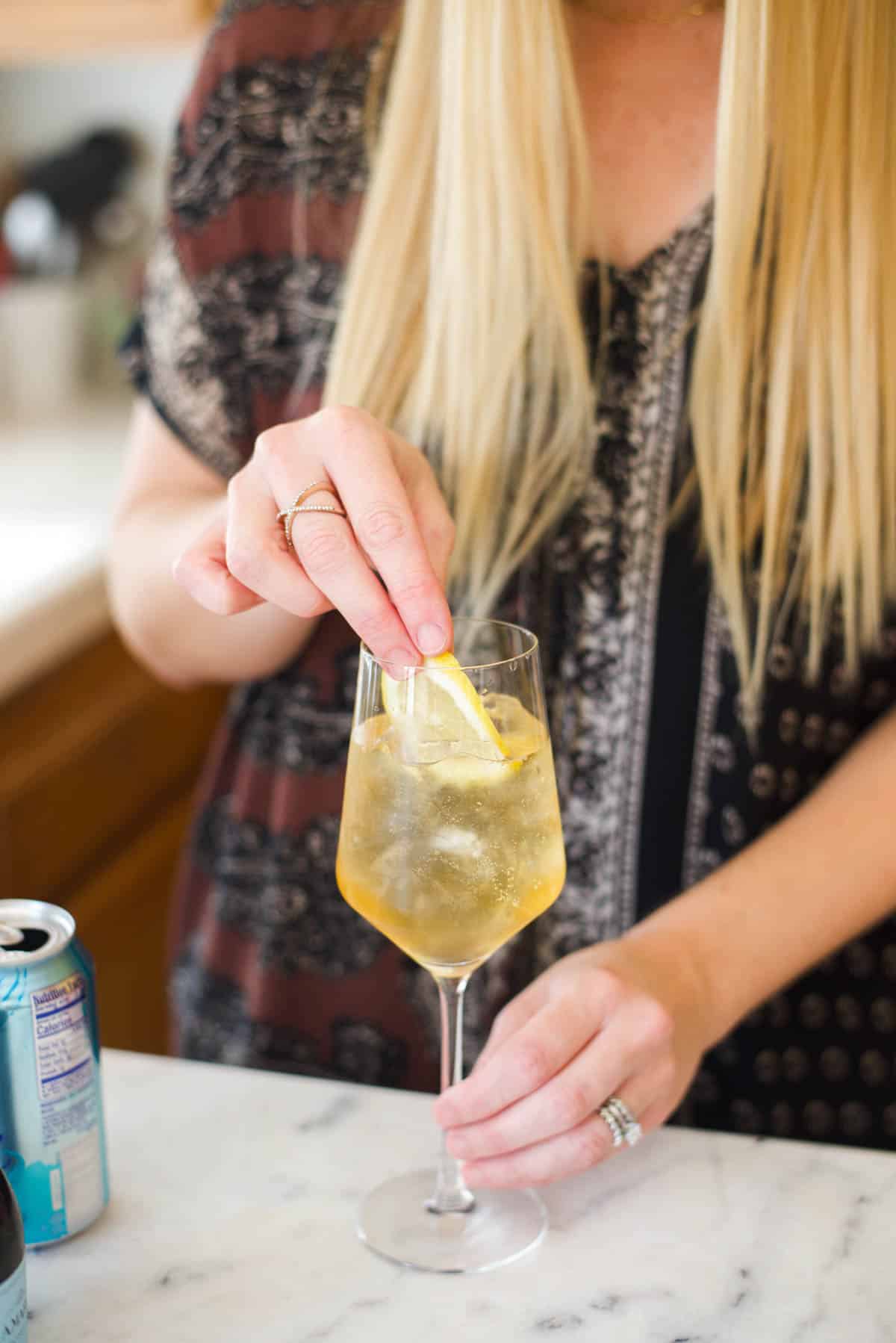 Woman adding lemon slice to a cocktail in a wine glass.