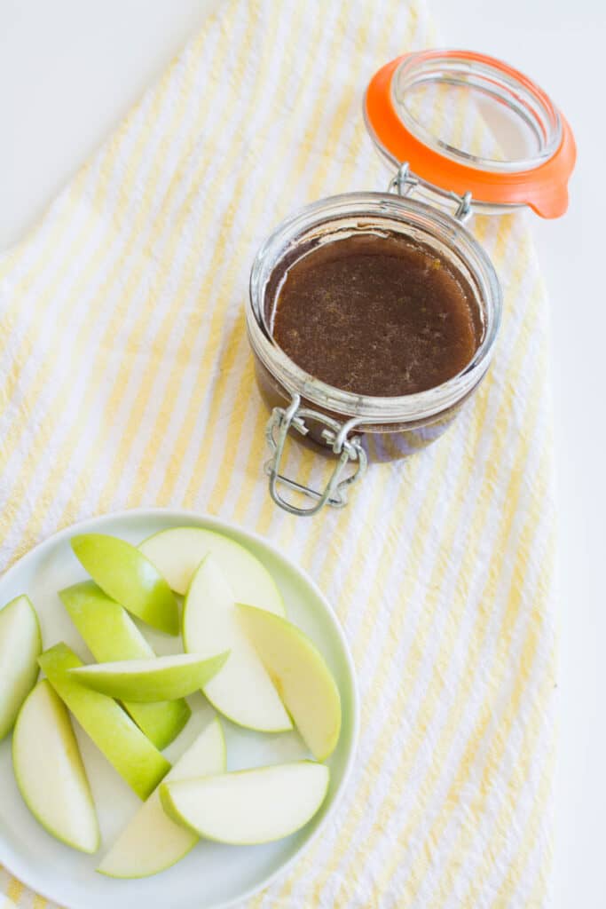 Green apples sliced on a plate next to a jar with honey apple dip in it.