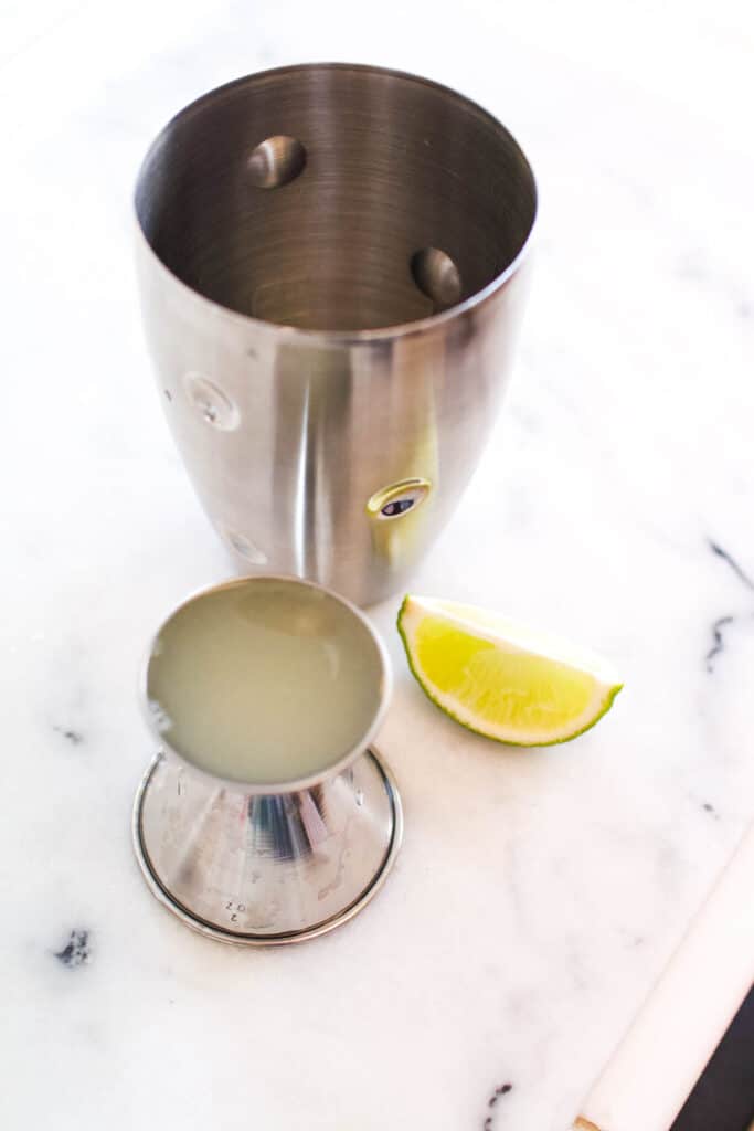A cocktail shaker on a counter next to a jigger of lime juice.