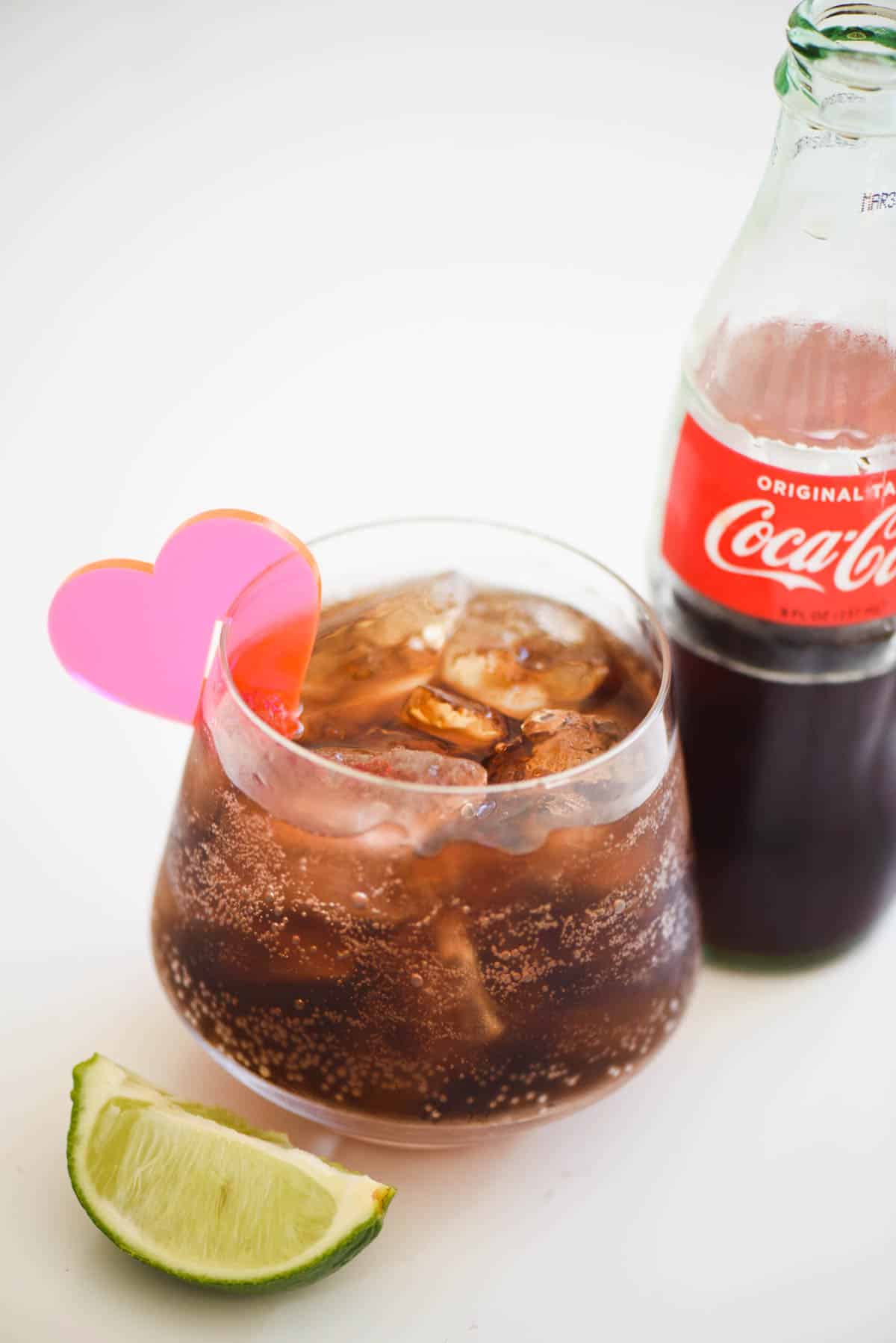 A close up of a glass of coke and tequila and a garnish of lime.