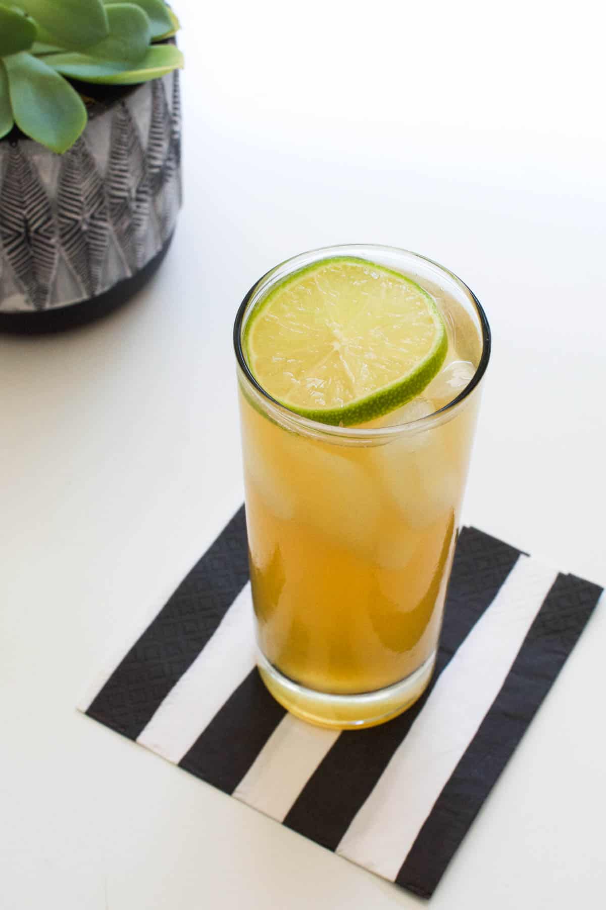 Shot of the top of a cocktail glass with a dark and stormy drink and lime garnish.