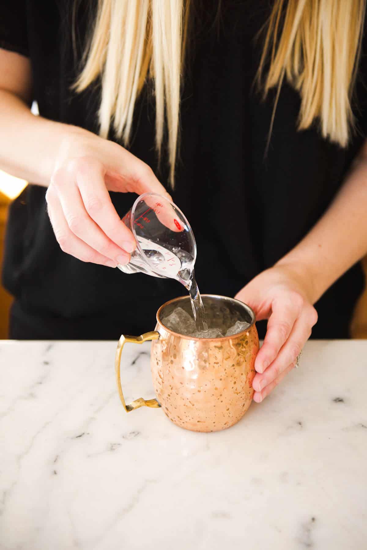 Adding the vodka to the copper mug to make the Blueberry Moscow Mule cocktail. 