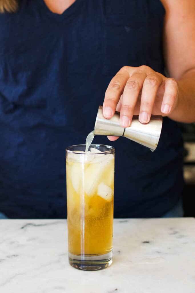 A woman pouring fresh lime juice into a cocktail glass from a jigger.