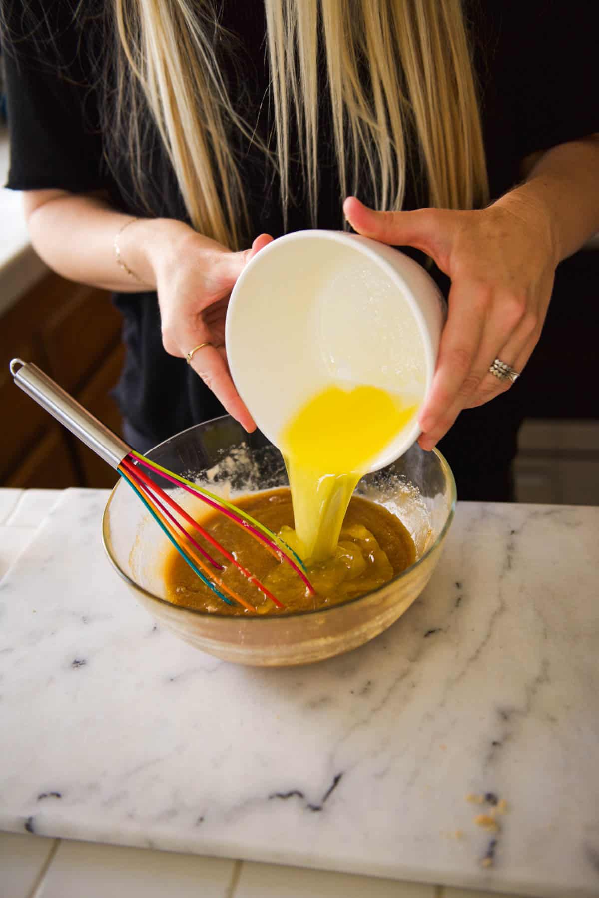 A woman pouring melted butter into a brown sugar pie mixture.