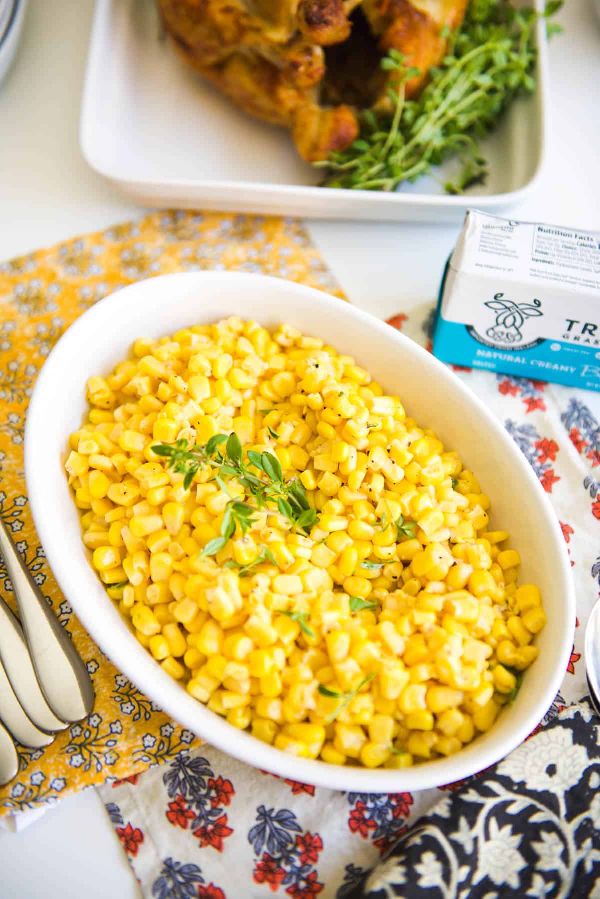 White serving dish with a corn side dish topped with fresh thyme.