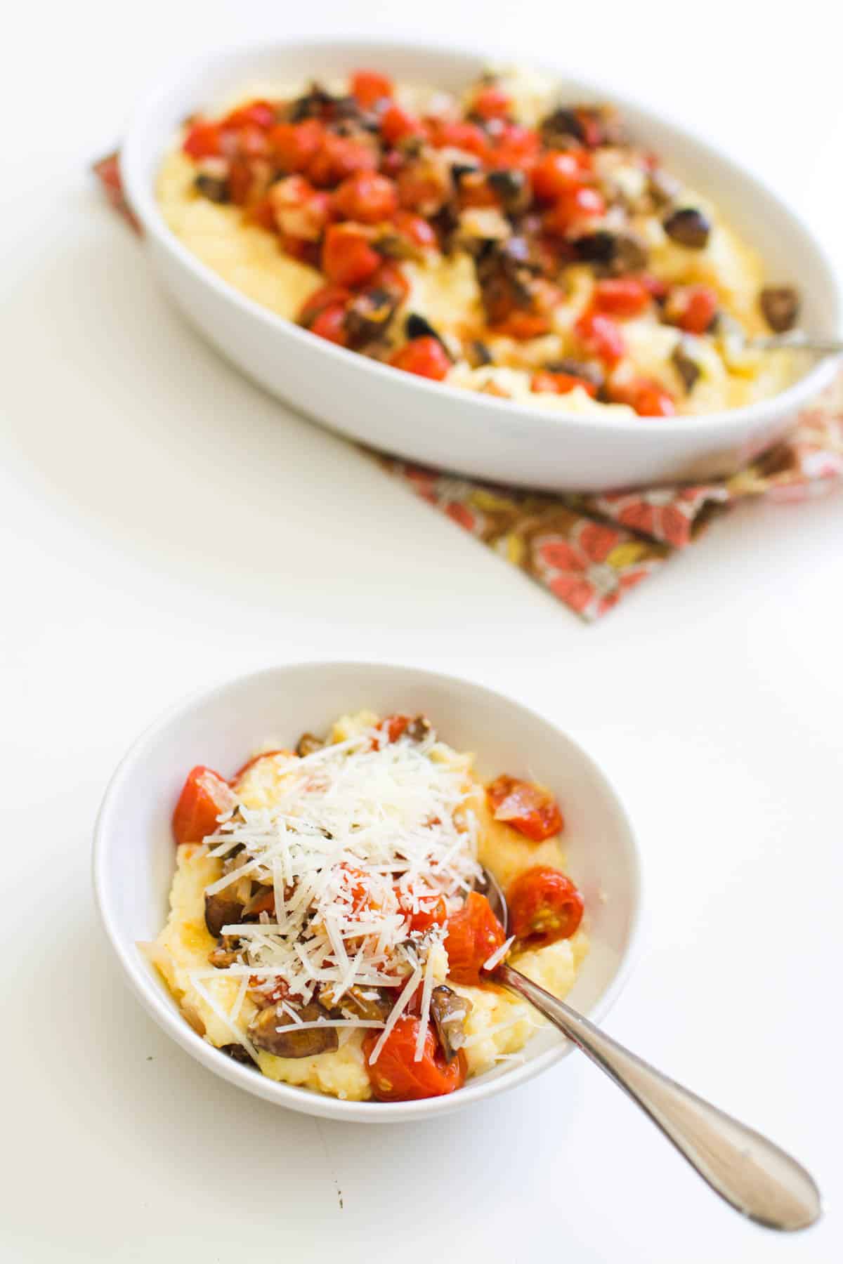 A small dish of polenta topped with roasted mushrooms and tomatoes and parmesan cheese.
