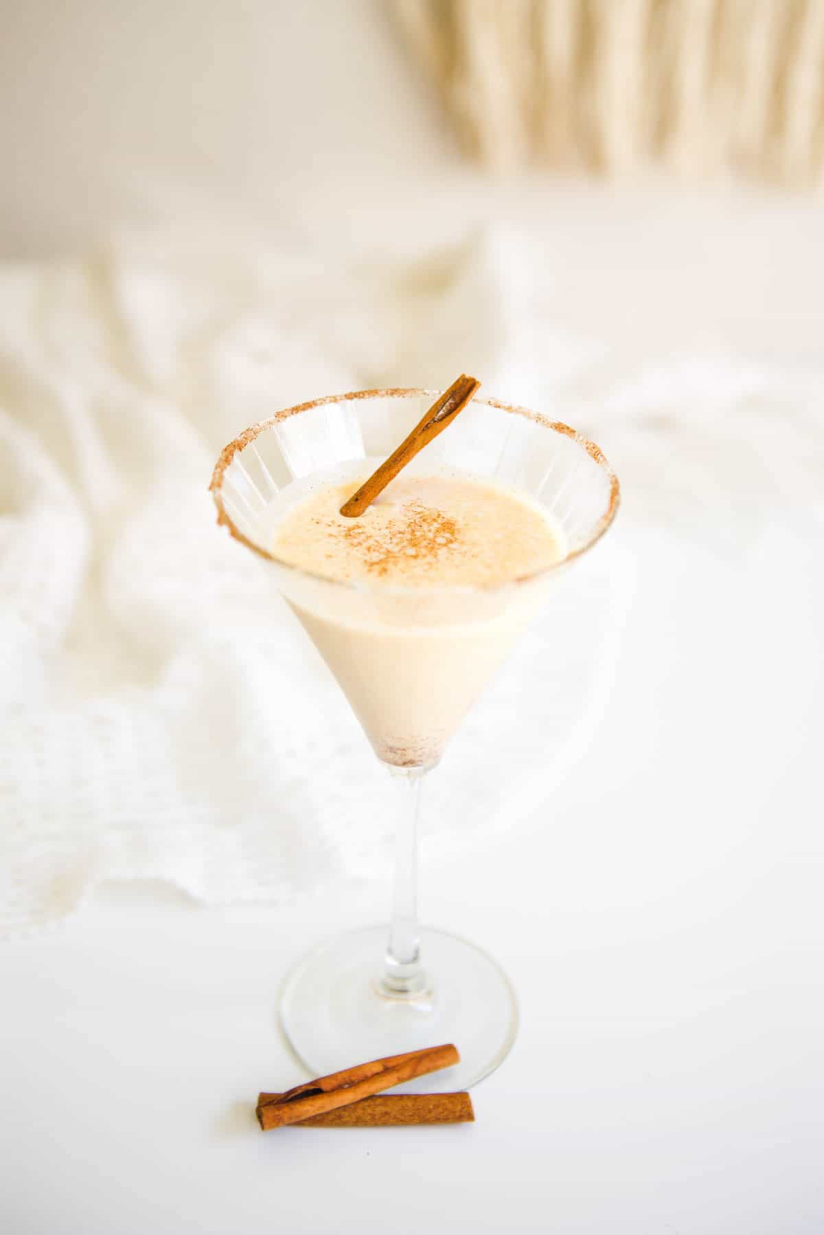 A pumpkin martini in a martini glass on a table with cinnamon sticks near the base.