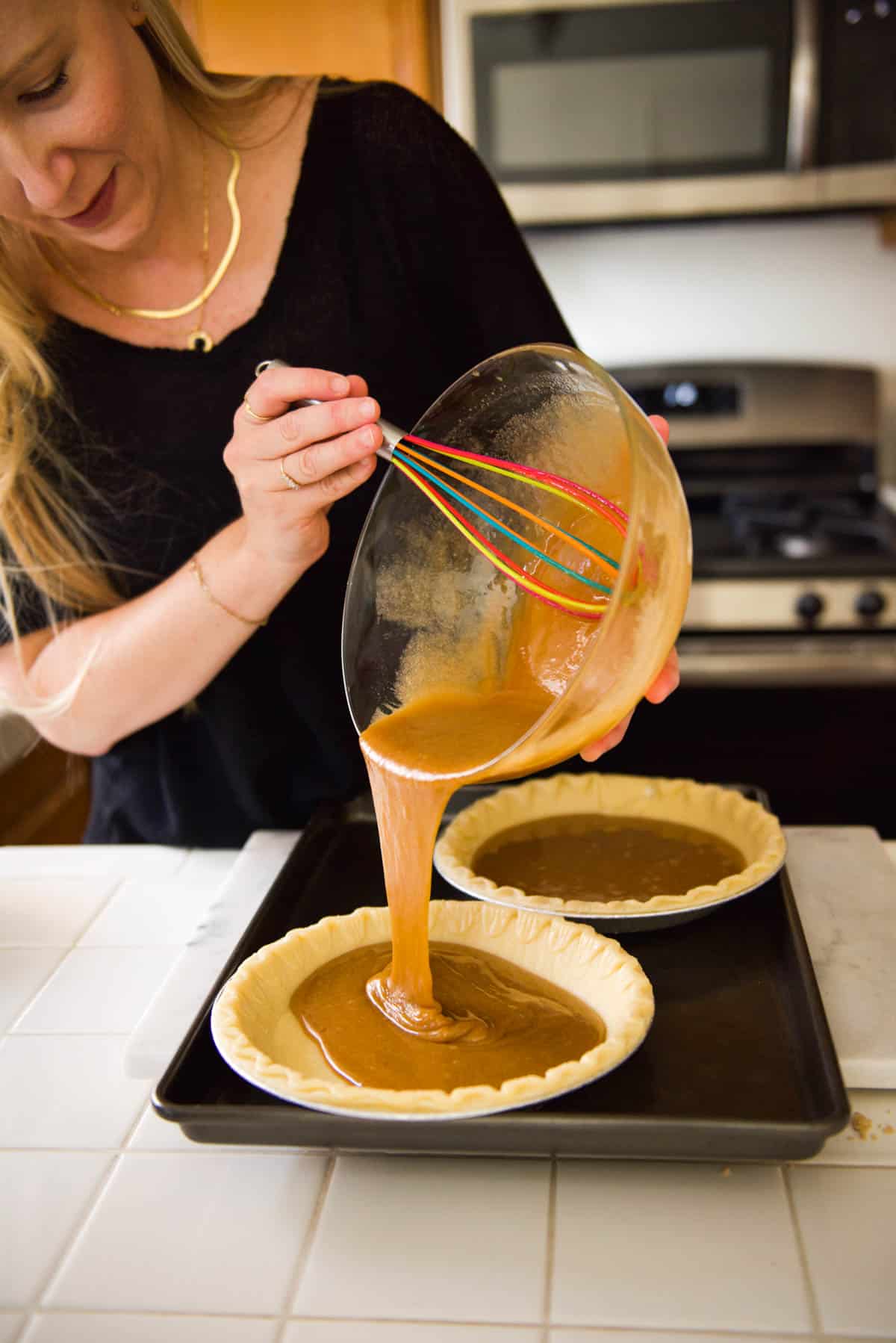 Woman pouring pie batter into crusts on a cookie sheet.