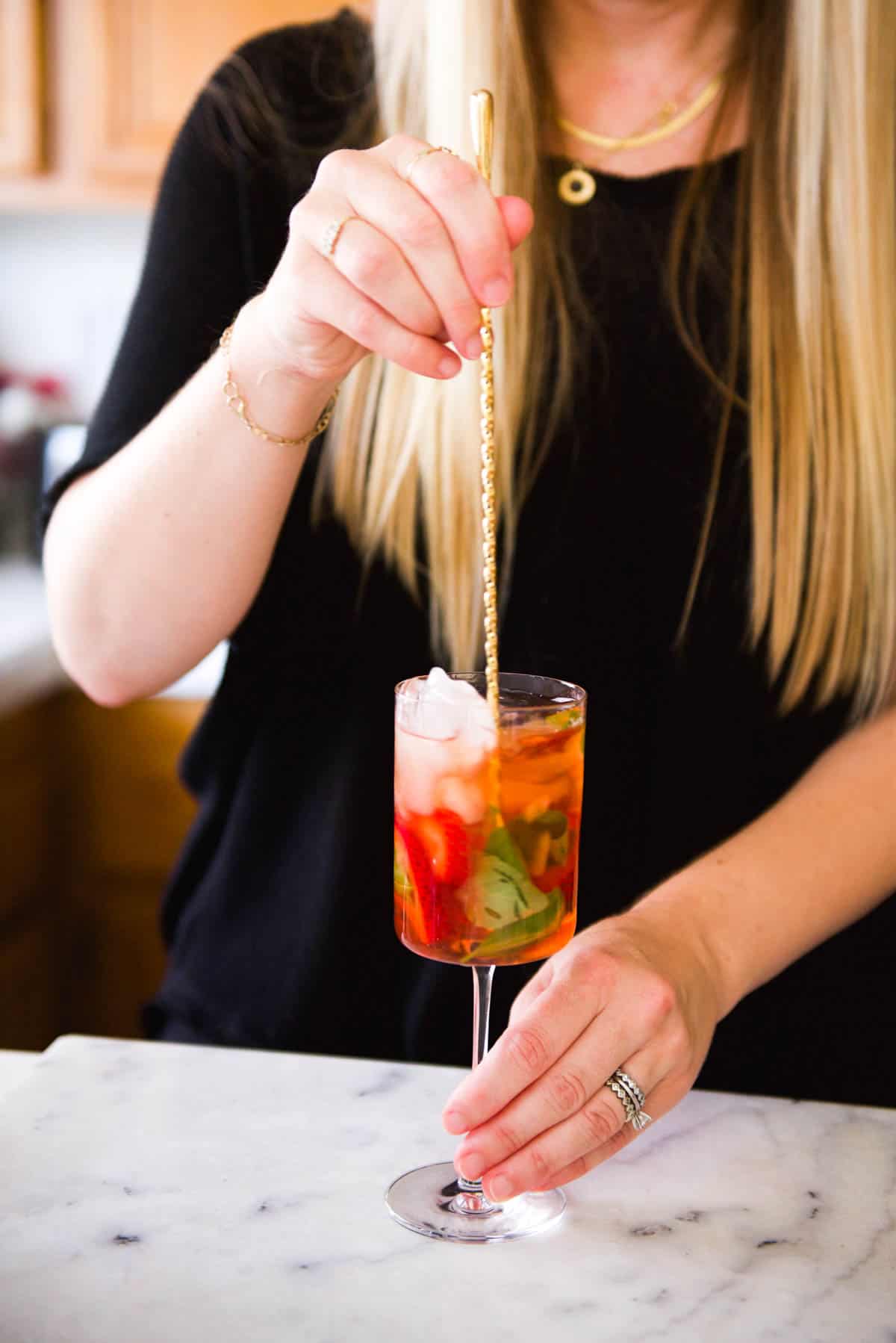 Woman stirring a cocktail in a wine glass with a bar spoon.