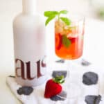 Close up of a bottle on a table with a cocktail served in a wine glass next to it.